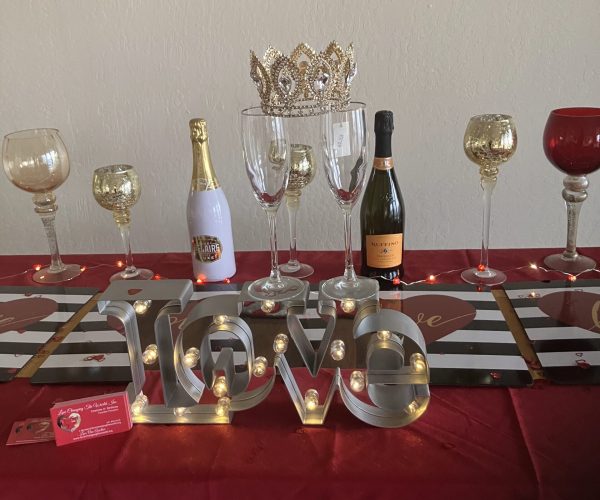 Event table decorated with red and gold theme, champagne bottles, glasses, and illuminated “LOVE” letters centerpiece.