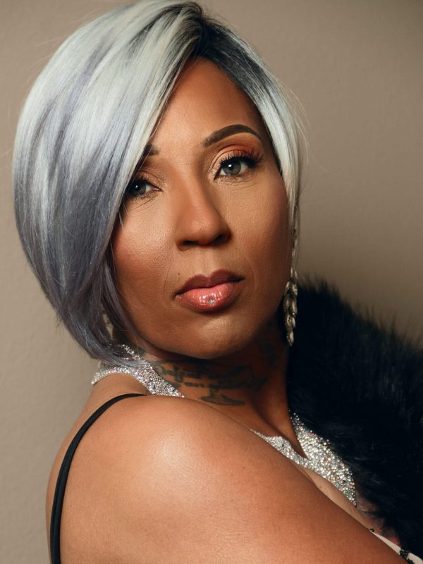 Professional portrait of a woman with silver hair, wearing formal attire and jewelry, looking confidently at the camera.